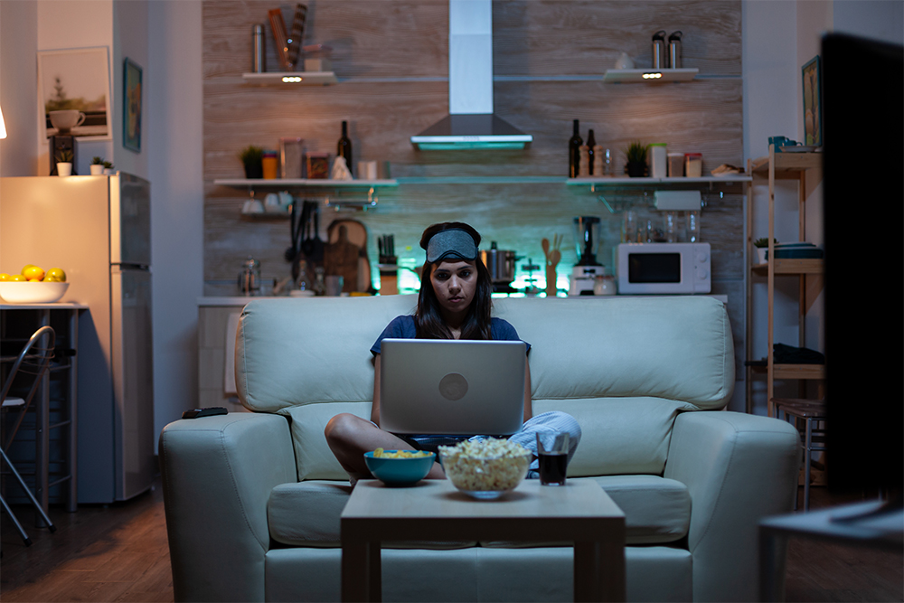 Woman Using Laptop at Night While Watching TV 
