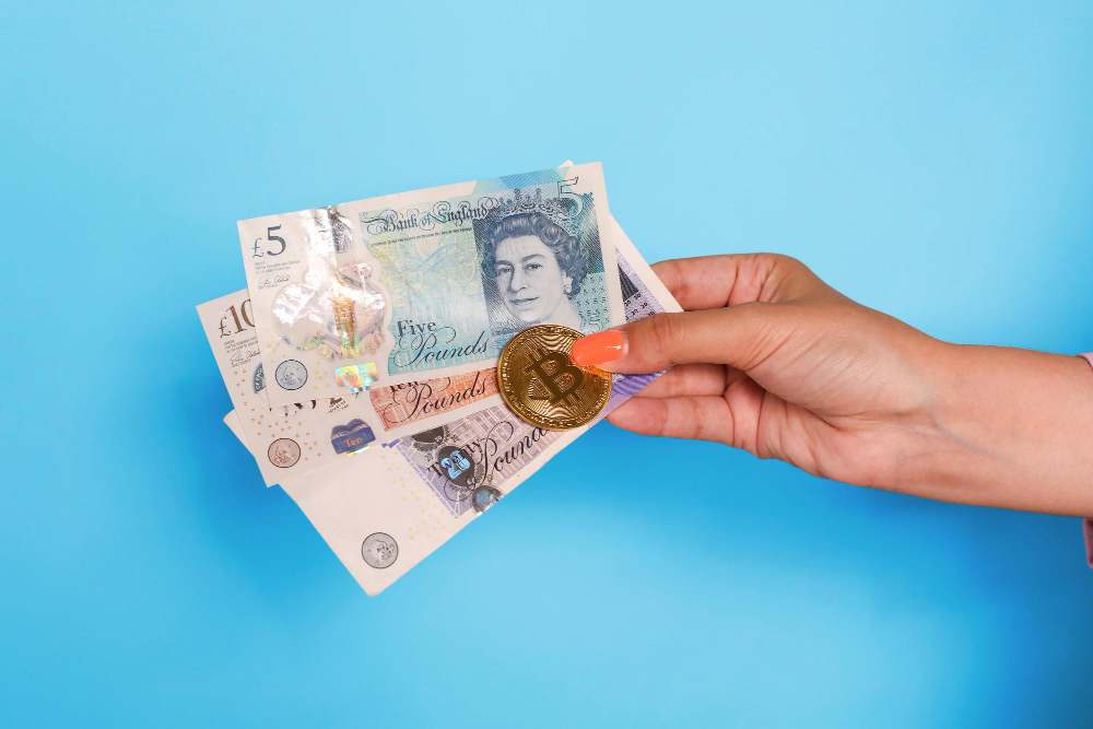 Hand Holding United Kingdom Pounds Banknotes and Bitcoin Over Blue Background