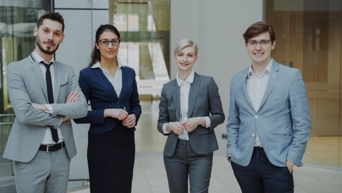 Four professionals in business attire stand together. young professionals, tech office, hiring