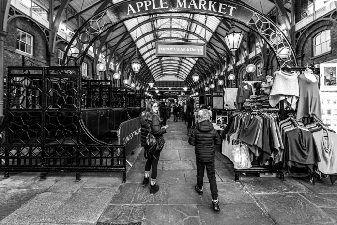 grayscale photo of man in black jacket and pants walking on sidewalk merchant terminal, point of sale, apple tap to pay