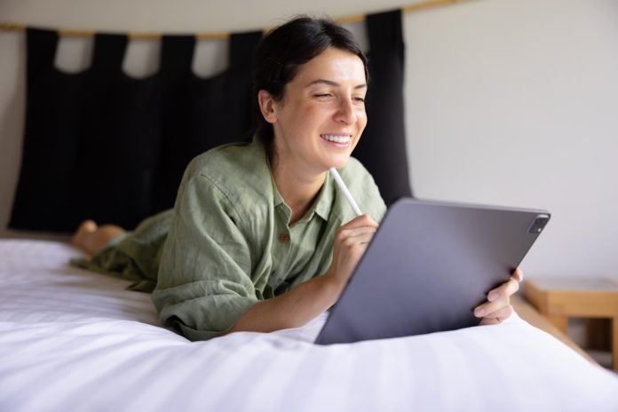a woman laying on a bed using a laptop computer hotel search, online booking, travel websites