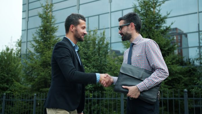 Two businessmen shaking hands outside modern building fintech, partnerships, handshake, technology collaboration