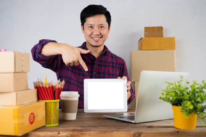 a man pointing at a laptop screen on a desk happy customer, package delivery, ecommerce success