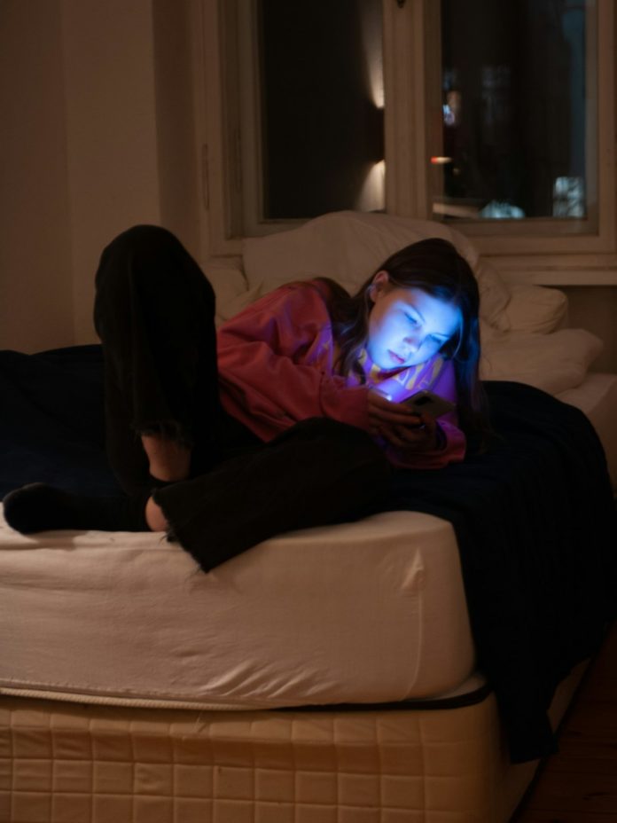 a woman laying on top of a bed in a room person scrolling phone in bed, glowing smartphone screen, night time anxiety