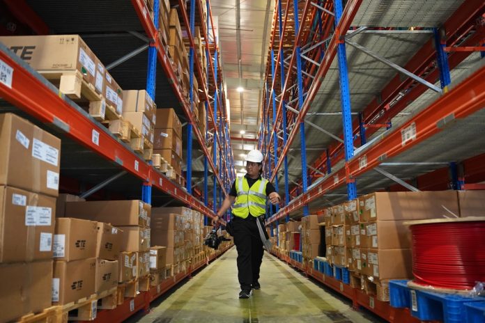 Man in reflective vest walks down warehouse aisle. warehouse shelves, ecommerce inventory, order packing