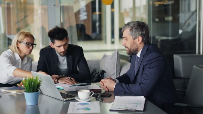 a group of people sitting around a table enterprise financial reporting dashboard, compliance documents, accounting team meeting
