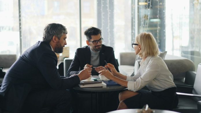 a group of people sitting around a table small business team meeting, reviewing testimonials, discussing marketing strategy