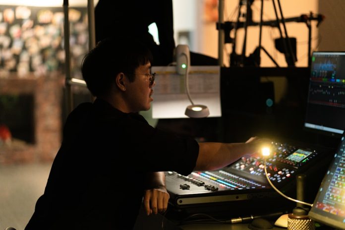 A person adjusting controls on a sound mixing board. enterprise video production studio, professional camera setup, broadcast control room, streaming server racks