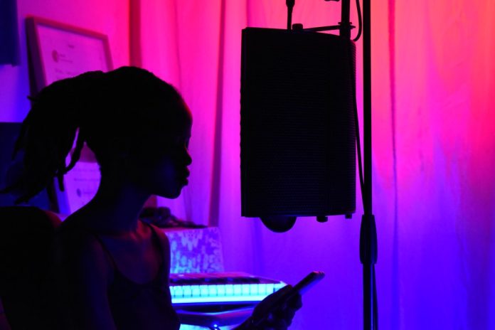woman in black tank top standing near black microphone stand person using singing app, smartphone screen pitch graph, vocal practice indoor