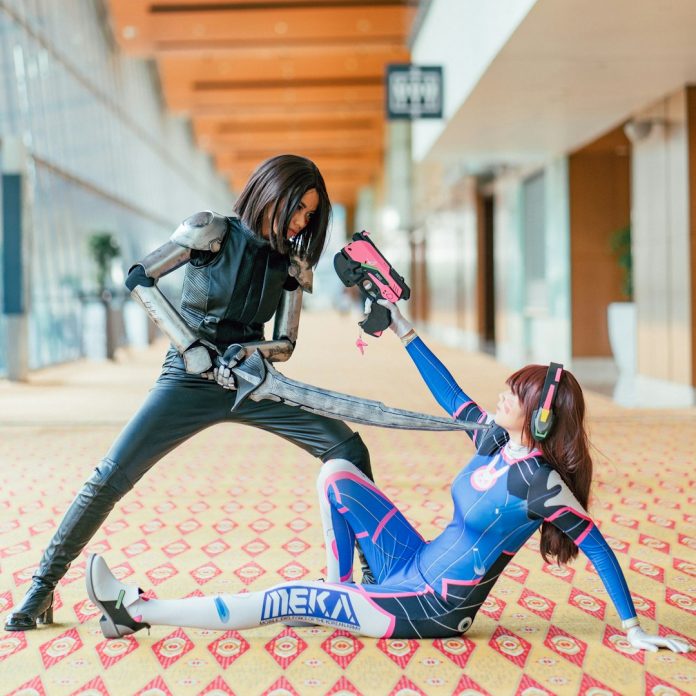 woman pointing sword to another woman cosplay team video call, shared digital design screen, armor prototype fitting