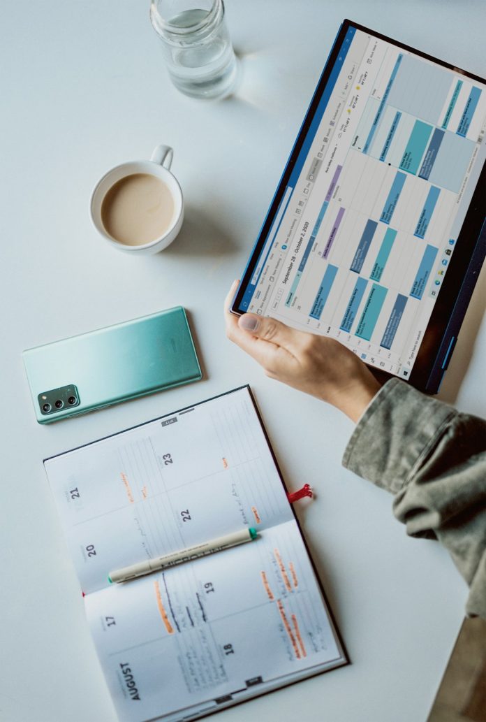 person holding ipad near white ceramic mug and laptop content calendar social media planning